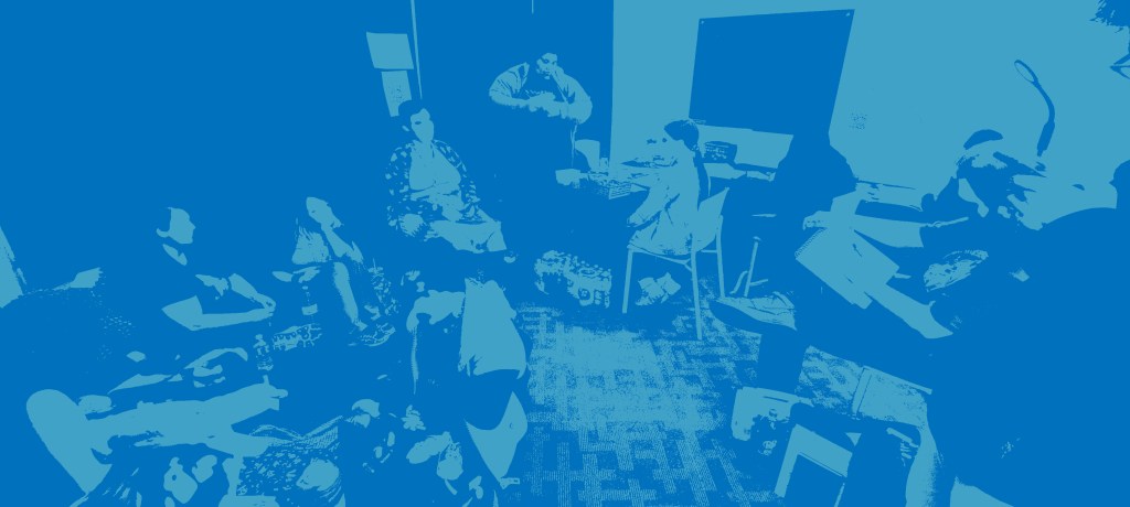 Photograph of several people sitting around a room talking, drawing, and stimming. Some are on the floor on cushions, others are in chairs. 